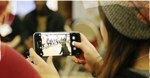 Student is using a smartphone to record or take a picture of a group of people. The scene is captured on the phone's screen.